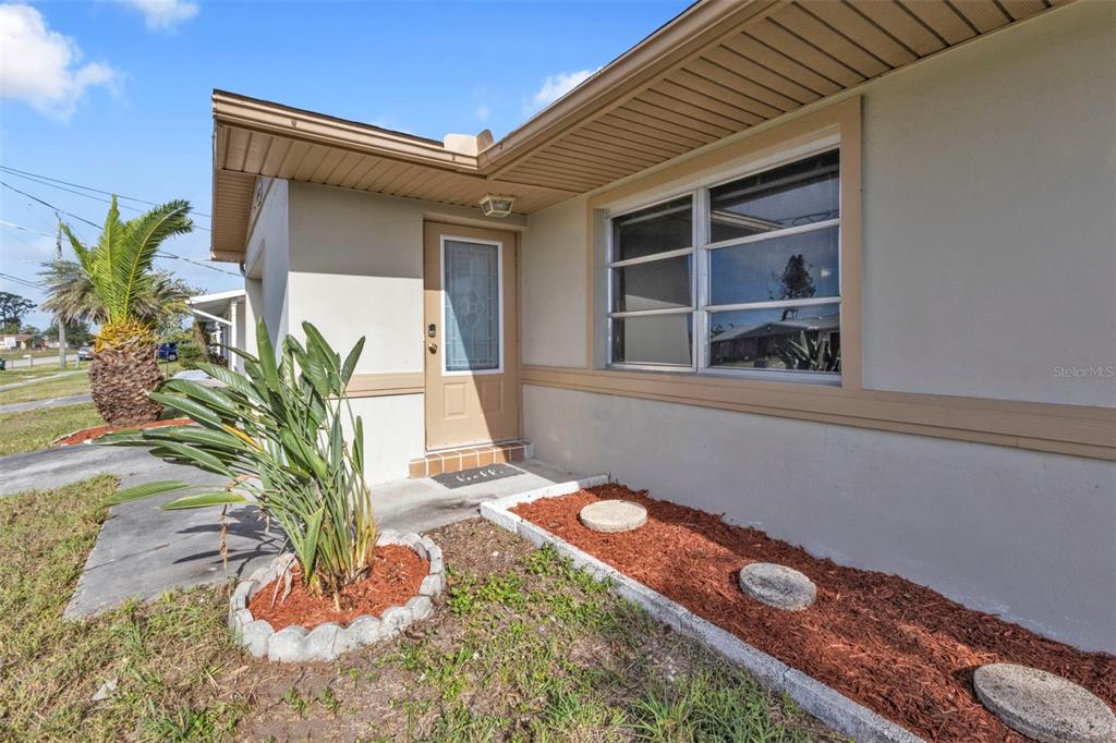 The exterior of a house features a tan door, a window, and a landscaped garden bed — 8172 TRIONFO AVENUE, NORTH PORT, FL