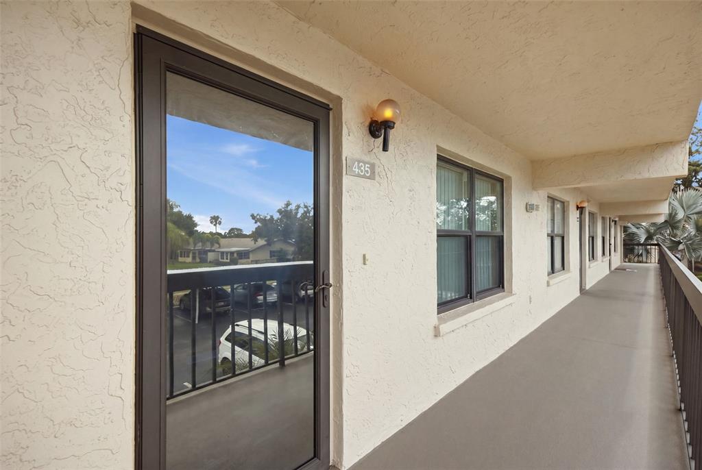 An exterior view of a building walkway featuring a door numbered 435 and windows — 435 30TH AVENUE W UNIT D206, BRADENTON, FL