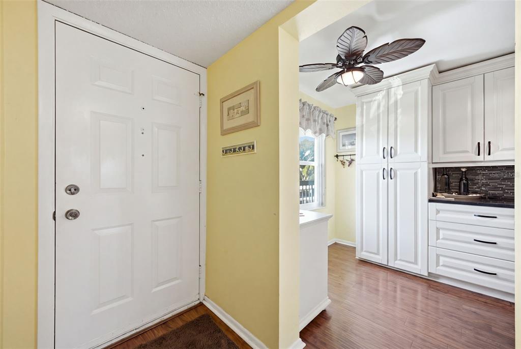 A bright entryway with a white door, yellow walls, wood flooring, and white kitchen cabinetry — 435 30TH AVENUE W UNIT D206, BRADENTON, FL