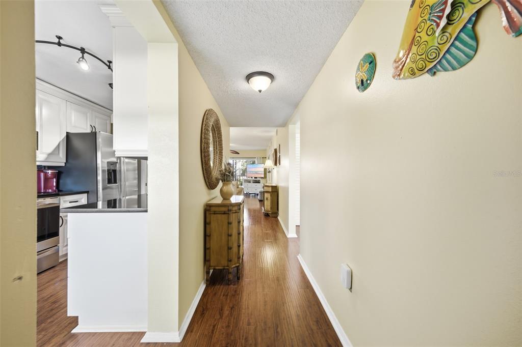 A hallway with wood-look flooring leads from a kitchen toward a living area — 435 30TH AVENUE W UNIT D206, BRADENTON, FL