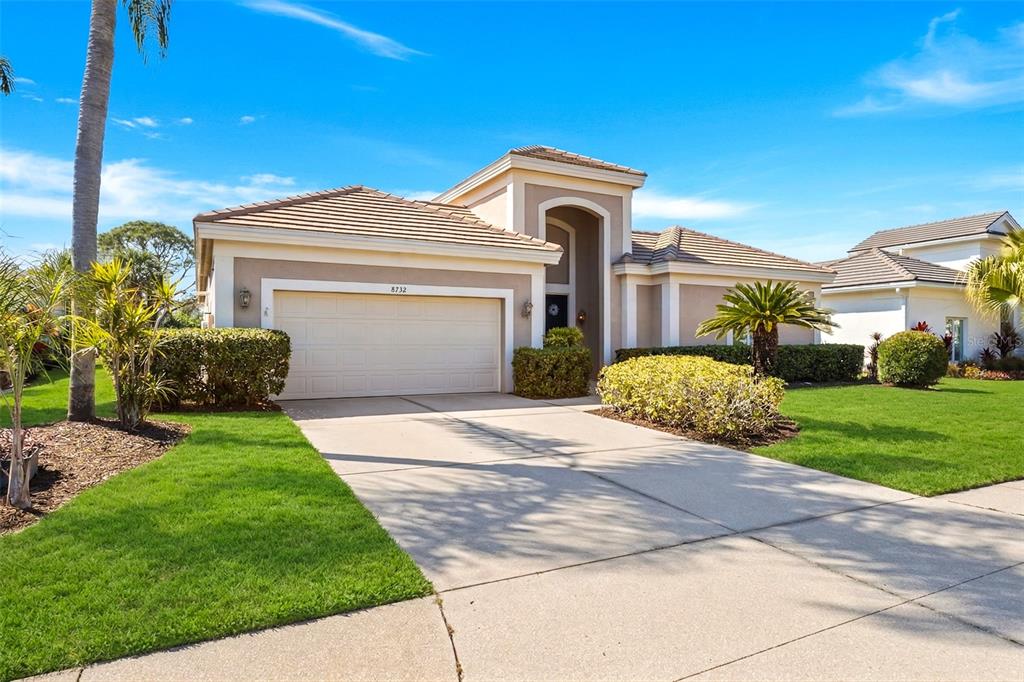 A single-story house with a beige stucco exterior, a tile roof, and a two-car garage — 8732 54TH AVENUE E, BRADENTON, FL