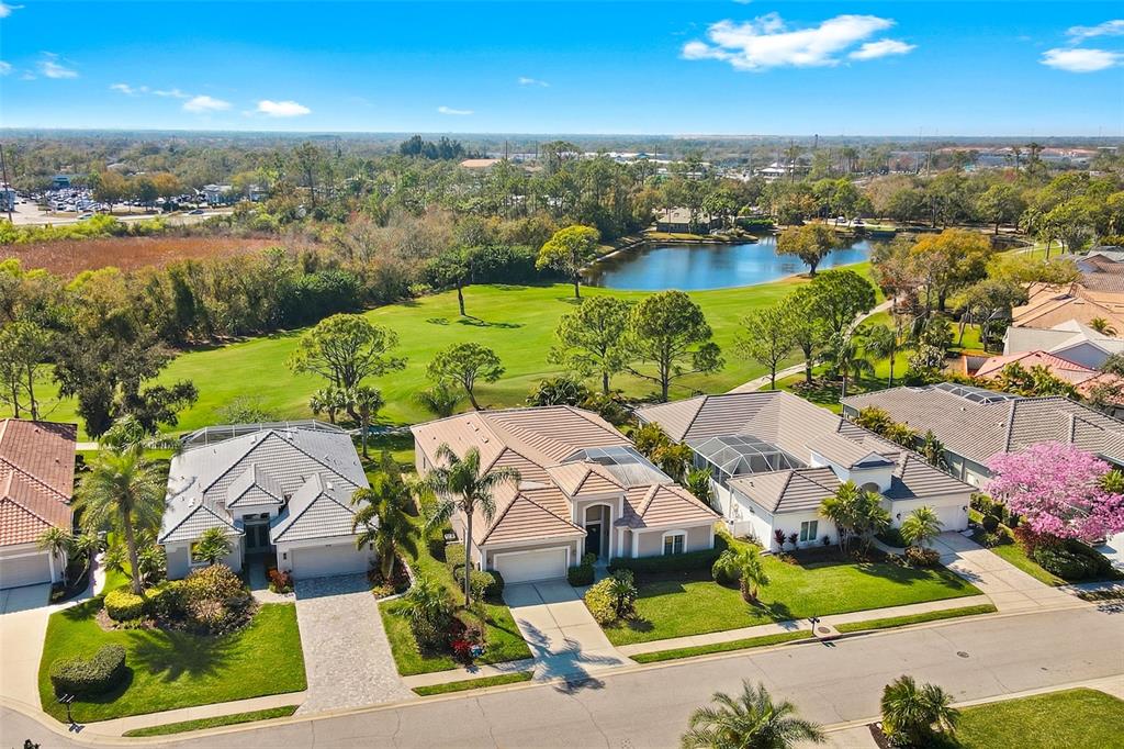 An aerial view shows three suburban houses with tiled roofs bordering a golf course and pond — 8732 54TH AVENUE E, BRADENTON, FL