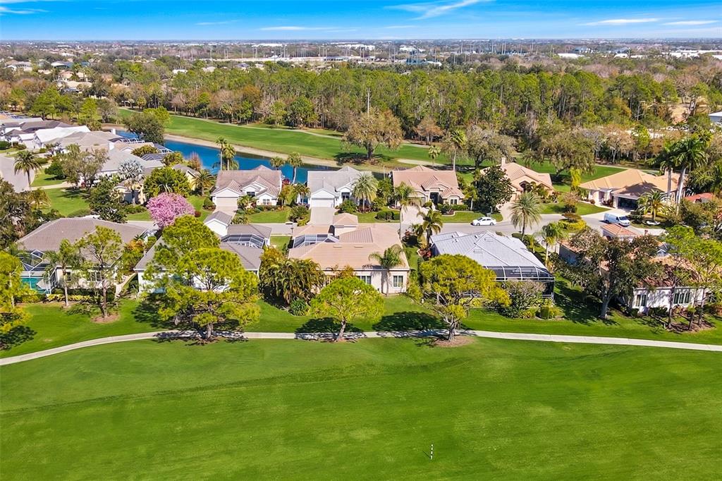 An aerial view of suburban houses bordering a golf course with a pond in the background — 8732 54TH AVENUE E, BRADENTON, FL