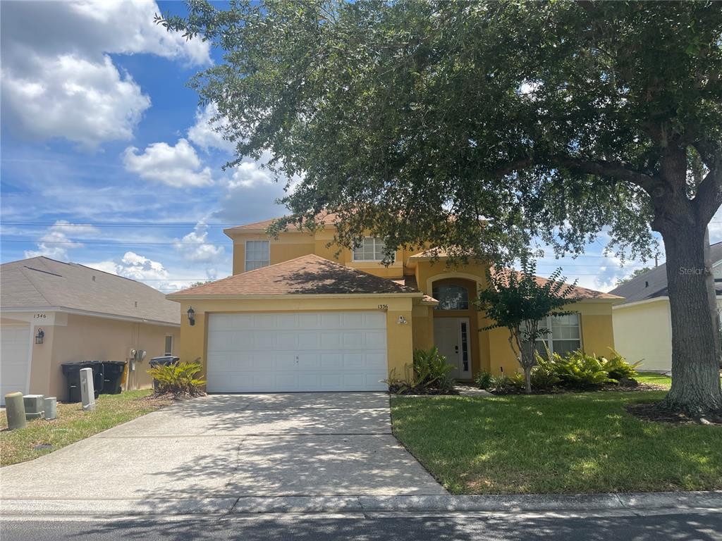 A two-story yellow house with a two-car garage and a large tree in front — 1336 CASTERTON CIRCLE, DAVENPORT, FL