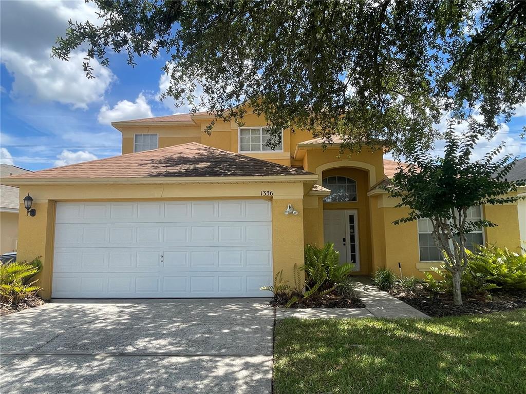 A two-story yellow stucco house features a two-car garage and a front entrance — 1336 CASTERTON CIRCLE, DAVENPORT, FL