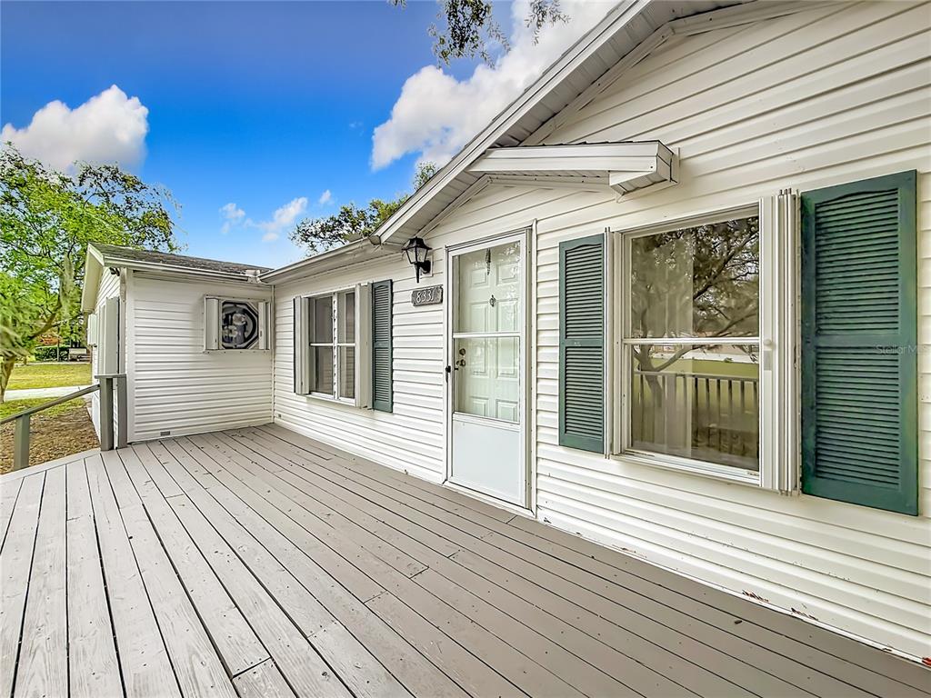 A white house exterior features a large wooden deck and green shutters on the windows — 8331 COUNTY ROAD 109, LADY LAKE, FL