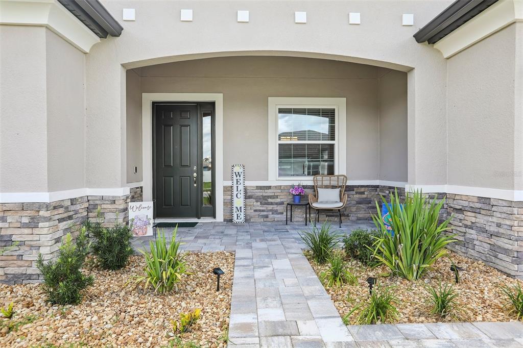 A stone-accented house exterior features a covered entryway, a dark front door, and landscaping — 902 TIERRA DR, SPRING HILL, FL