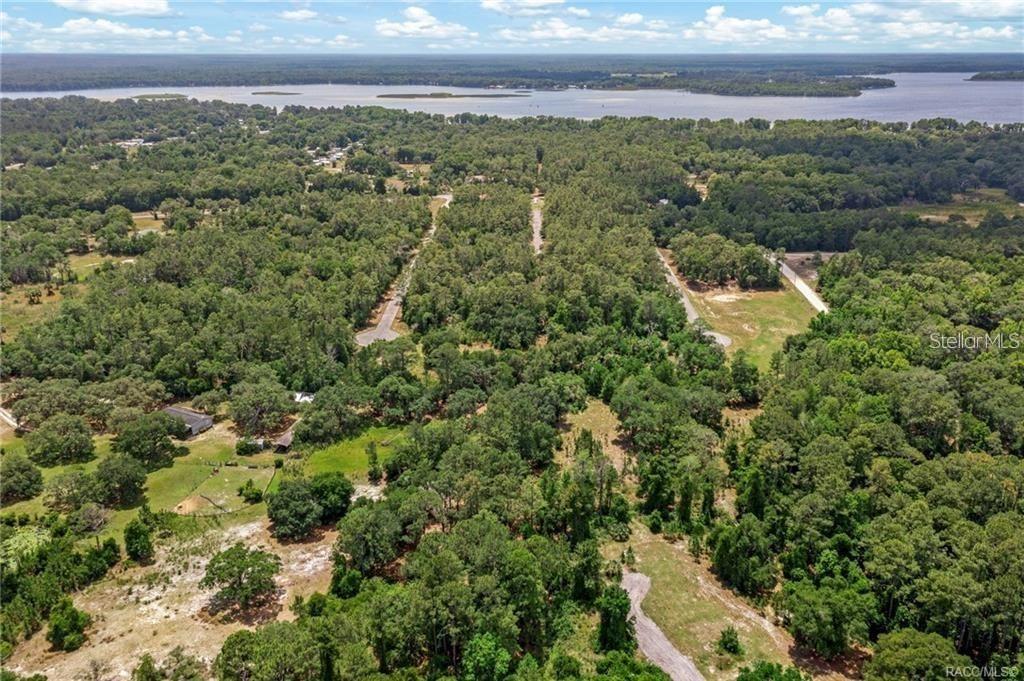 An aerial view shows a wooded landscape with dirt roads leading toward a large lake — 11151 HWY 40 E, INGLIS, FL