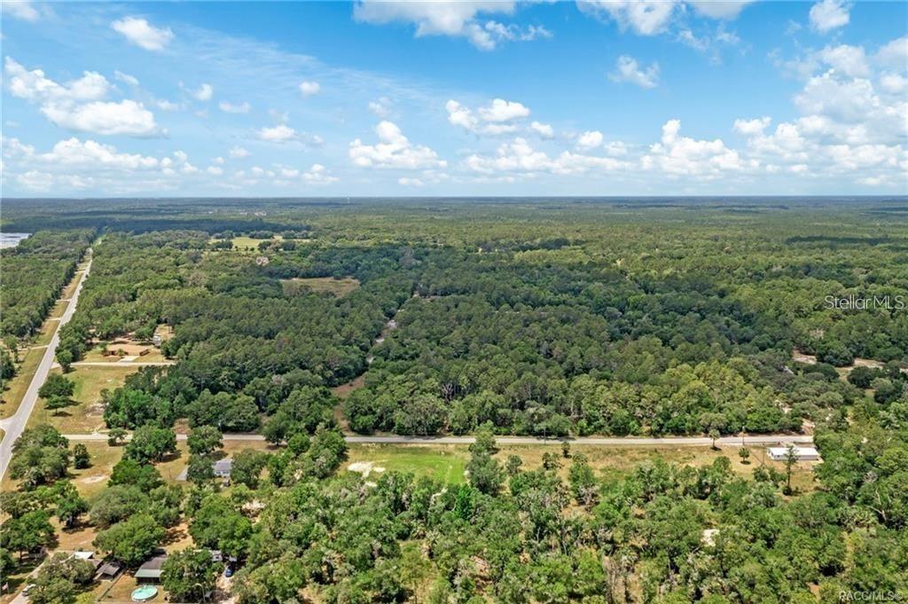 An aerial view shows a rural landscape with a road, scattered houses, and dense forest — 11151 HWY 40 E, INGLIS, FL