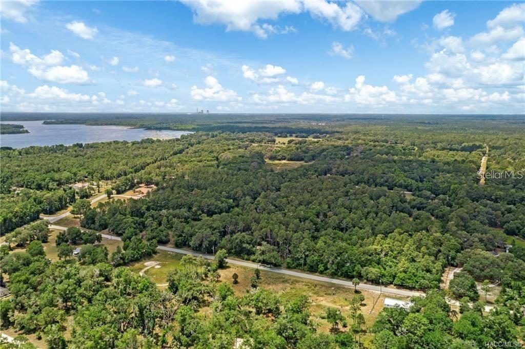 An aerial view shows a rural landscape with a road, dense forest, and a lake — 11151 HWY 40 E, INGLIS, FL