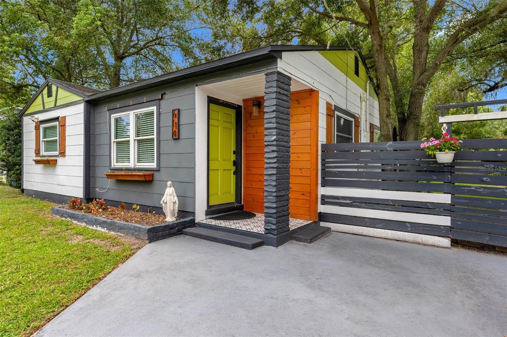 A small house exterior features a lime green door, grey siding, and a wooden porch wall — 6114 N 23RD STREET, TAMPA, FL