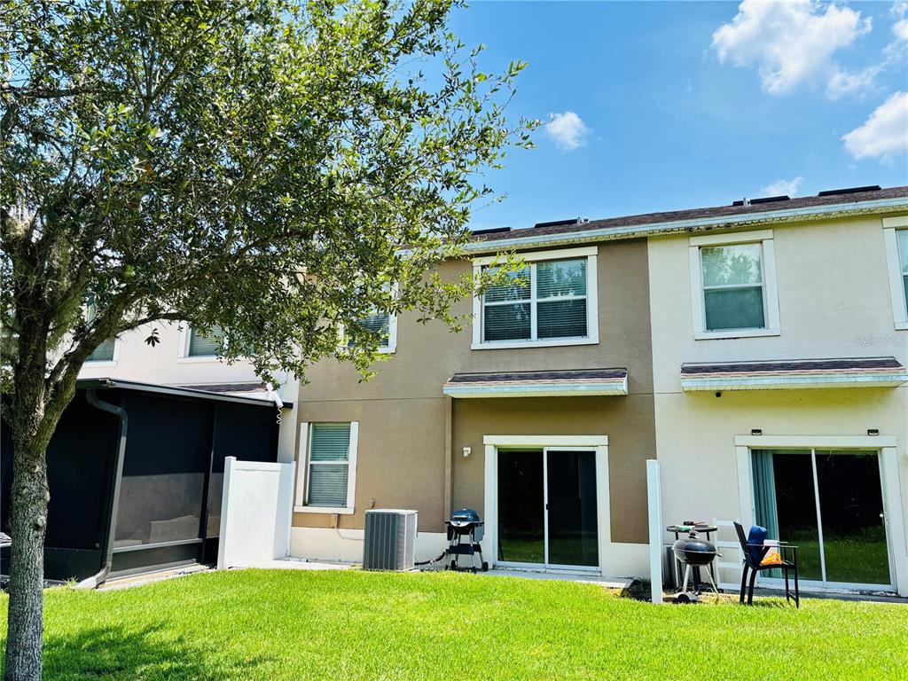 The exterior rear view of a two-story townhouse features a small lawn and patio area — 11155 SAVANNAH LANDING CIRCLE, ORLANDO, FL