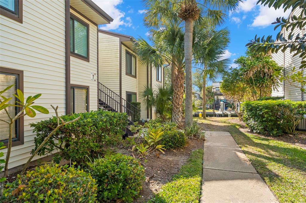 A concrete walkway leads past a two-story apartment building with light siding and palm trees — 412 MOORINGS COVE DRIVE UNIT 7H, TARPON SPRINGS, FL