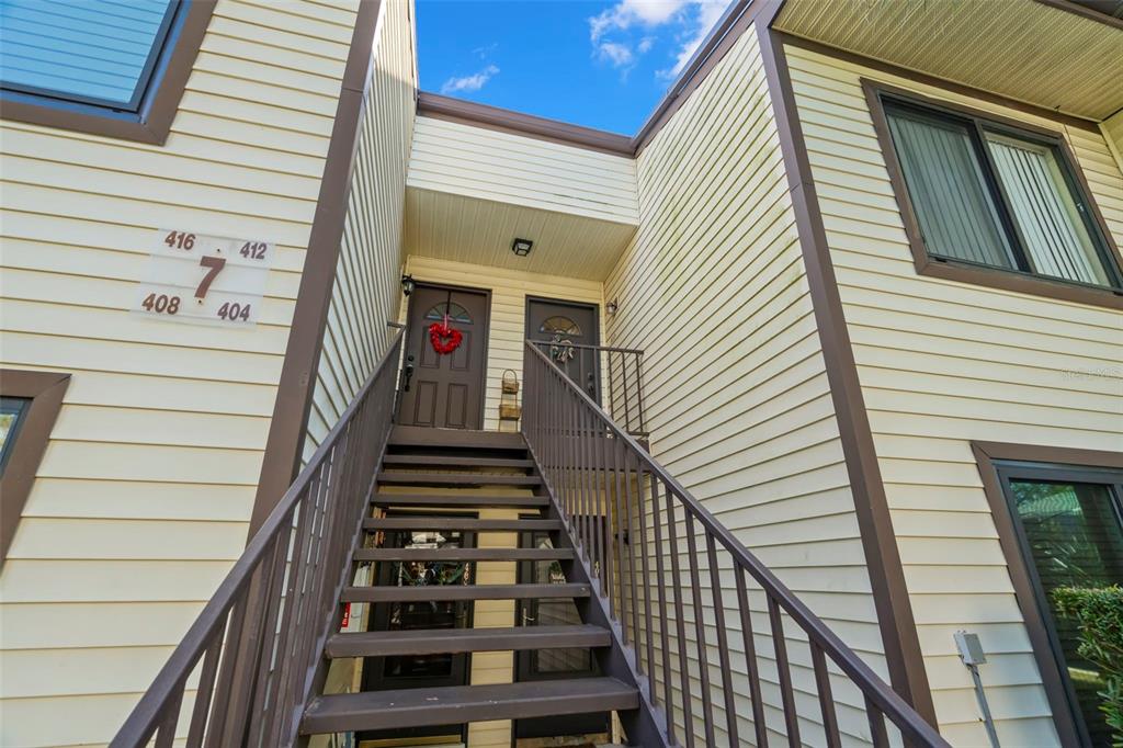 An exterior view of a two-story apartment building with stairs leading to upper-level unit doors — 412 MOORINGS COVE DRIVE UNIT 7H, TARPON SPRINGS, FL