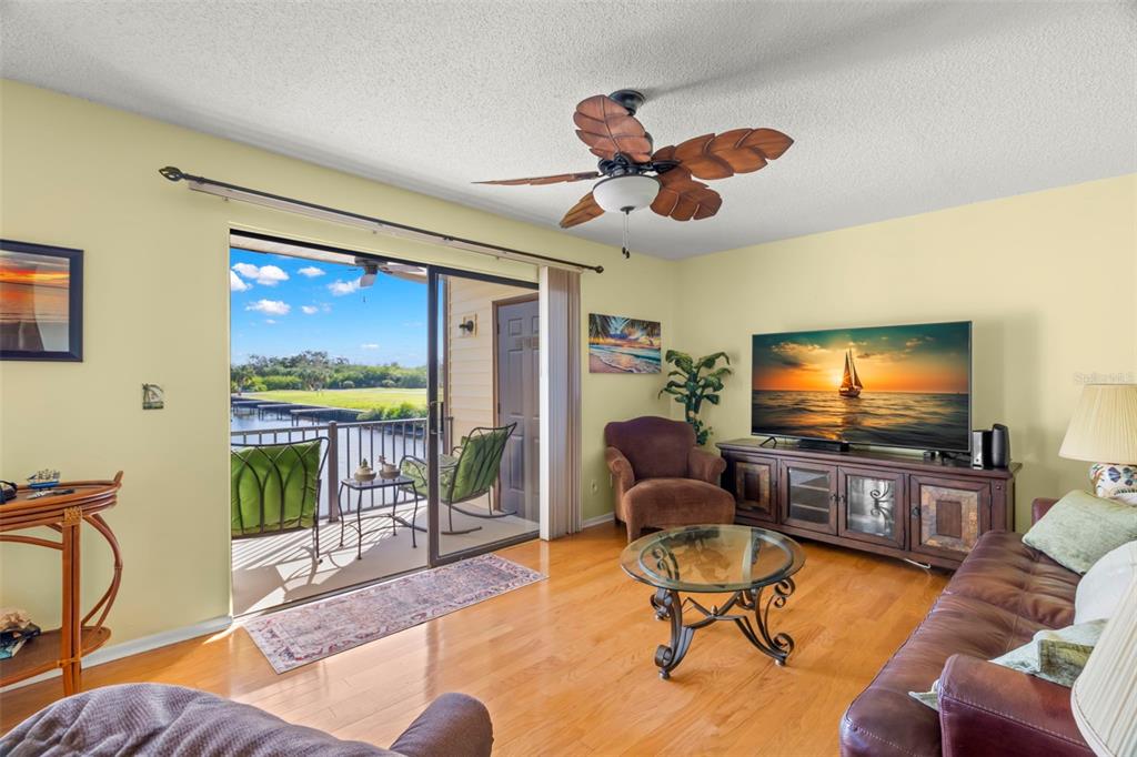 A living room with hardwood floors, a ceiling fan, and a sliding door to a balcony — 412 MOORINGS COVE DRIVE UNIT 7H, TARPON SPRINGS, FL