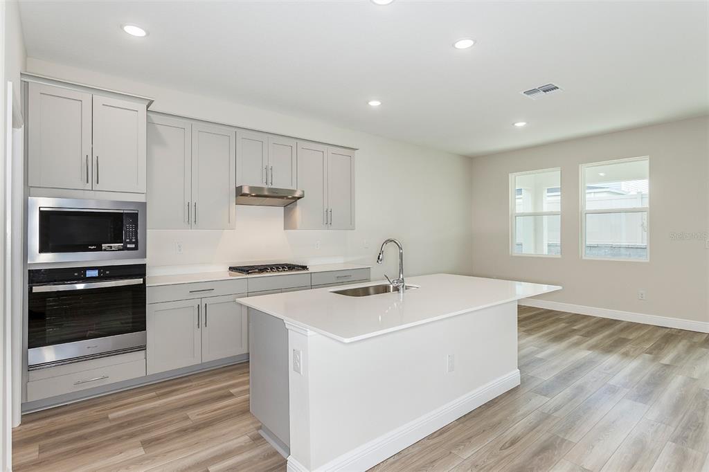 A modern kitchen features light gray cabinets, white countertops, a center island, and wood-look flooring — 33508 HAMMOCK BEACH WAY, DADE CITY, FL