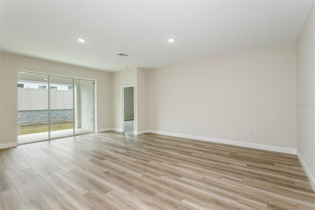 An empty room with light wood-look flooring, recessed lighting, and a sliding glass door — 33508 HAMMOCK BEACH WAY, DADE CITY, FL
