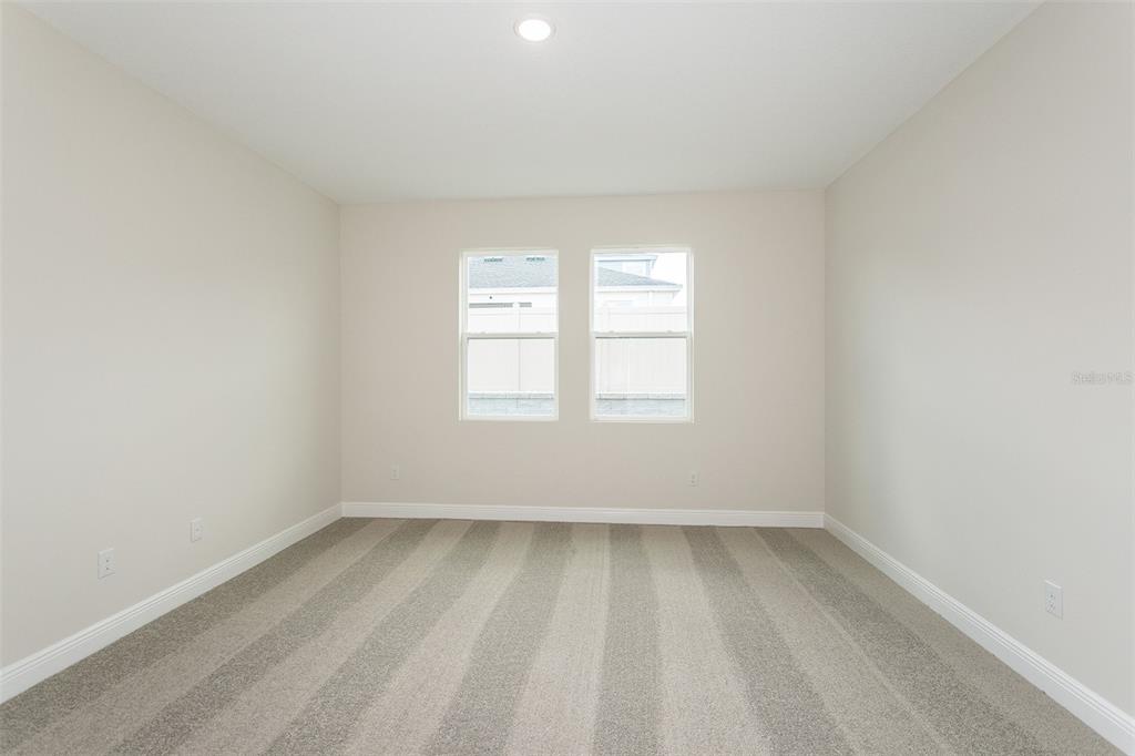 An empty bedroom features beige walls, white trim, and gray striped carpeting — 33508 HAMMOCK BEACH WAY, DADE CITY, FL