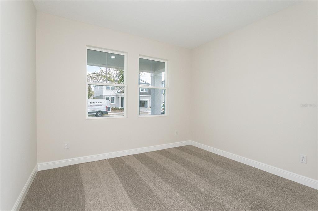 An empty room with beige walls, gray carpet, and two windows overlooking a street — 33508 HAMMOCK BEACH WAY, DADE CITY, FL