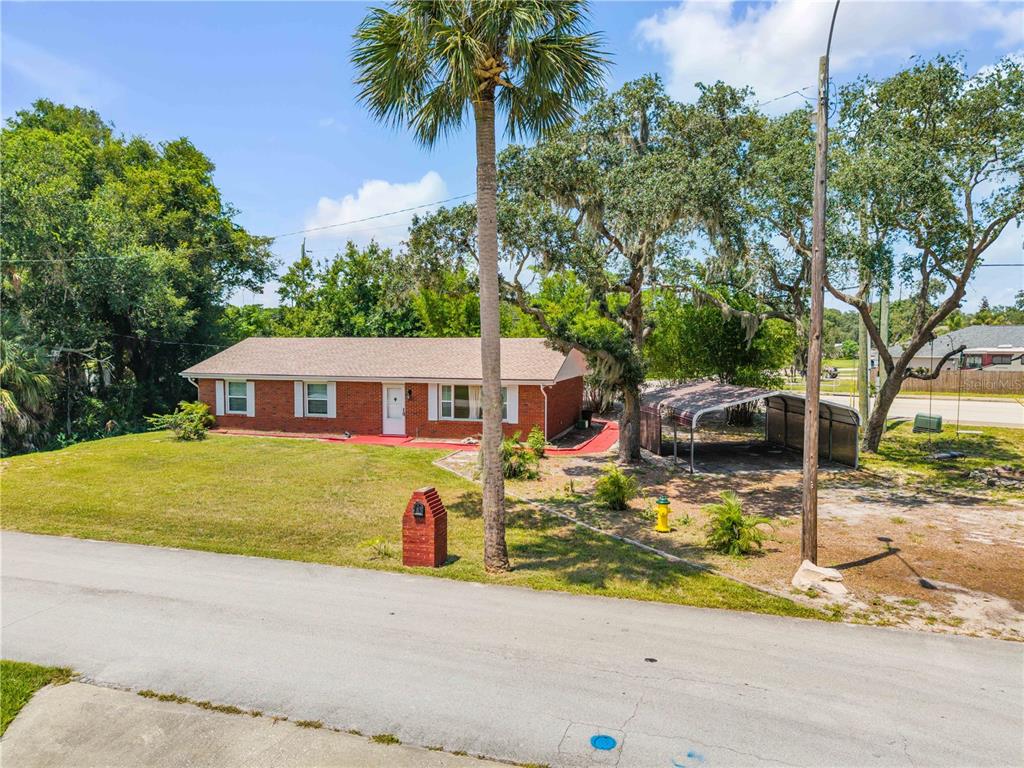A single-story red brick house with a metal carport sits on a grassy corner lot — 5680 PALM AVENUE, PORT ORANGE, FL