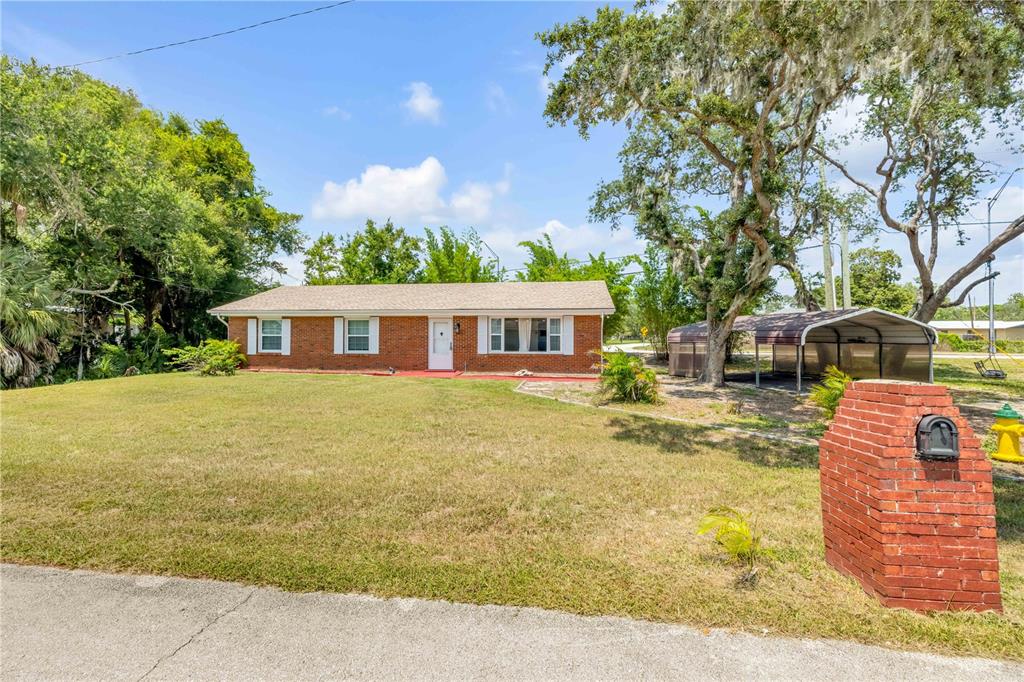 A single-story red brick house with a front lawn and a detached metal carport — 5680 PALM AVENUE, PORT ORANGE, FL