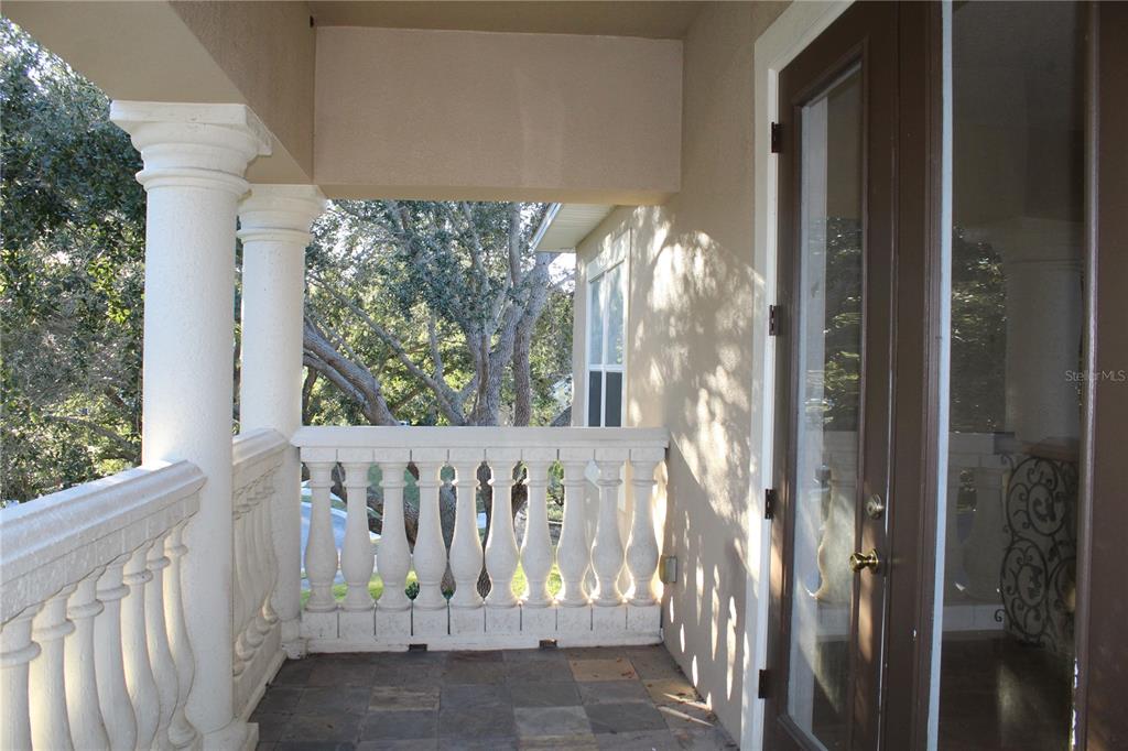 A covered balcony features stone tile flooring, white balustrades, a column, and a glass door — 13019 SUMMERLAKE WAY, CLERMONT, FL