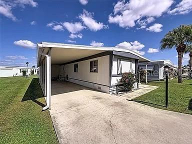 A white mobile home with a carport and a concrete driveway under a blue sky — 213 LAKESIDE RANCH CIRCLE, WINTER HAVEN, FL