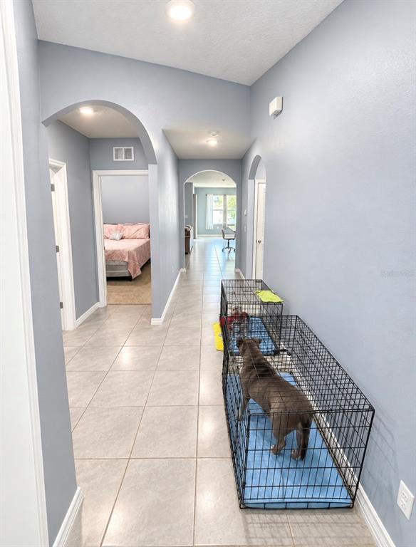 A tiled hallway features arched doorways, gray walls, and two dog crates containing dogs — 635 AUTUMN STREAM DRIVE, AUBURNDALE, FL
