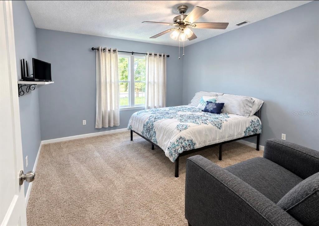 A bedroom with gray walls, a ceiling fan, a bed with pink bedding, and carpeted flooring — 635 AUTUMN STREAM DRIVE, AUBURNDALE, FL