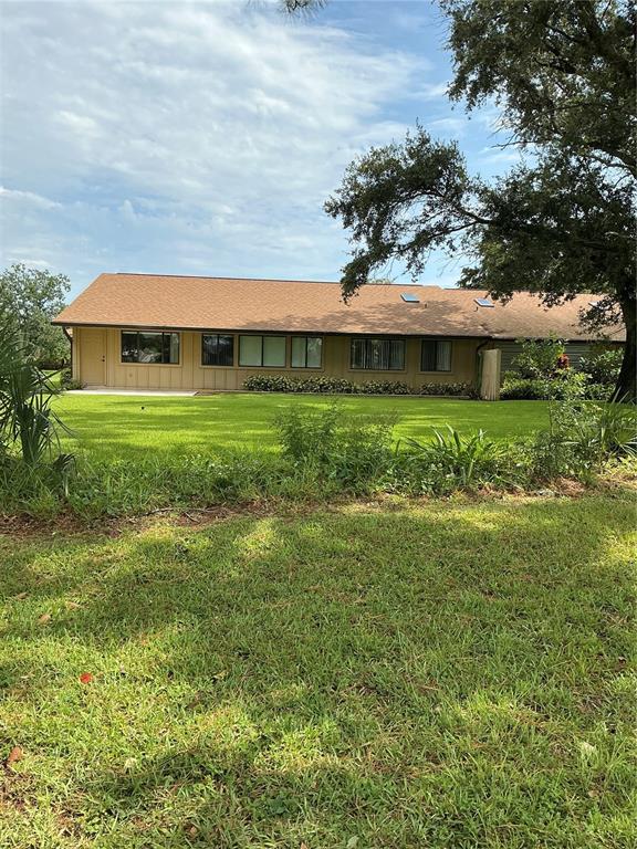 A single-story house with tan siding and a brown shingled roof sits on a lawn — 31 LAKE FAIRGREEN CIRCLE, NEW SMYRNA BEACH, FL