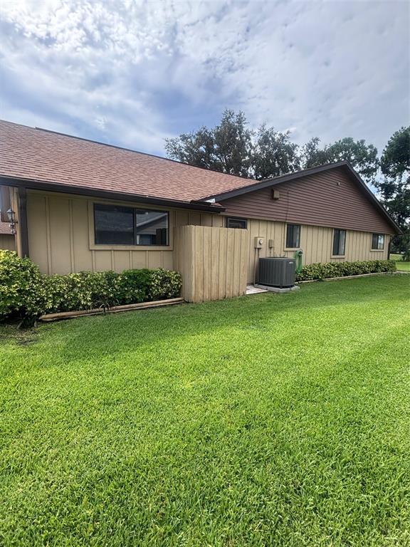 The exterior of a tan, single-story building features a wooden privacy screen and air conditioner — 31 LAKE FAIRGREEN CIRCLE, NEW SMYRNA BEACH, FL