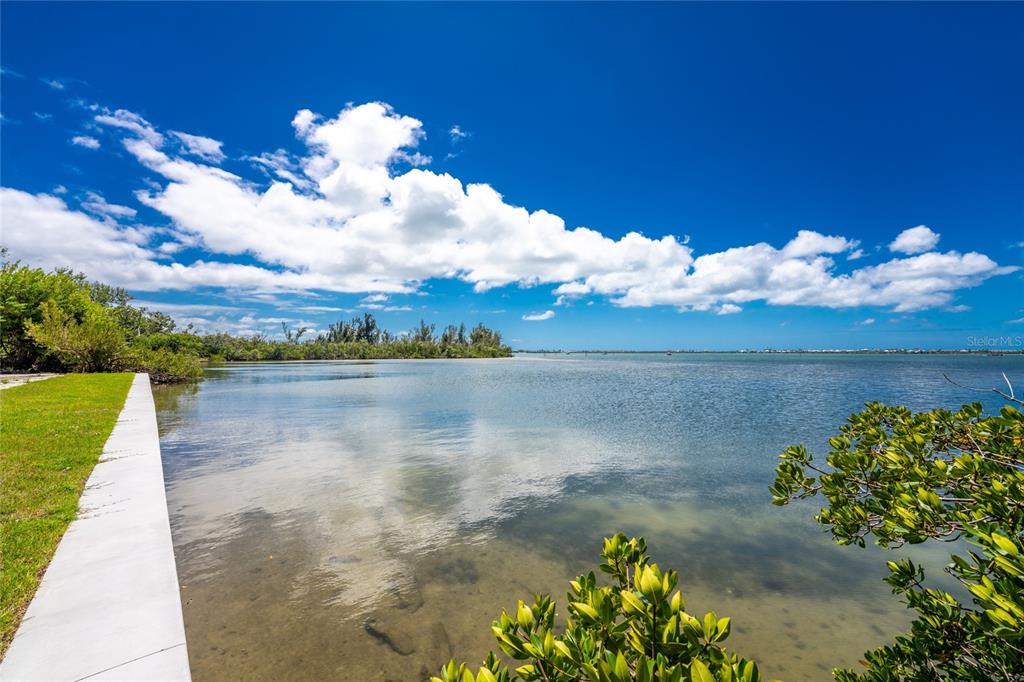 A concrete walkway borders a calm bay with mangroves under a bright, cloudy blue sky — 12500 PLACIDA ROAD, PLACIDA, FL