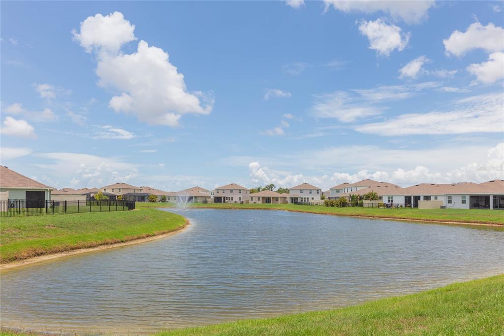 A pond with a fountain sits in front of several suburban houses under a blue sky — 10732 CHIPPEWA DRIVE, PARRISH, FL