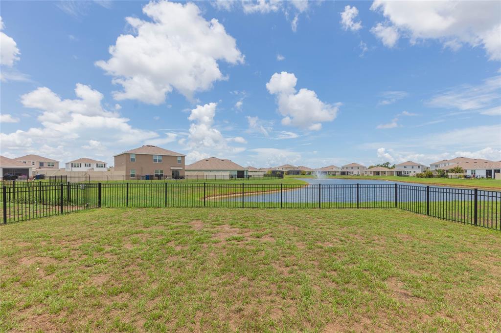A grassy backyard with a black metal fence overlooks a pond and suburban houses — 10732 CHIPPEWA DRIVE, PARRISH, FL