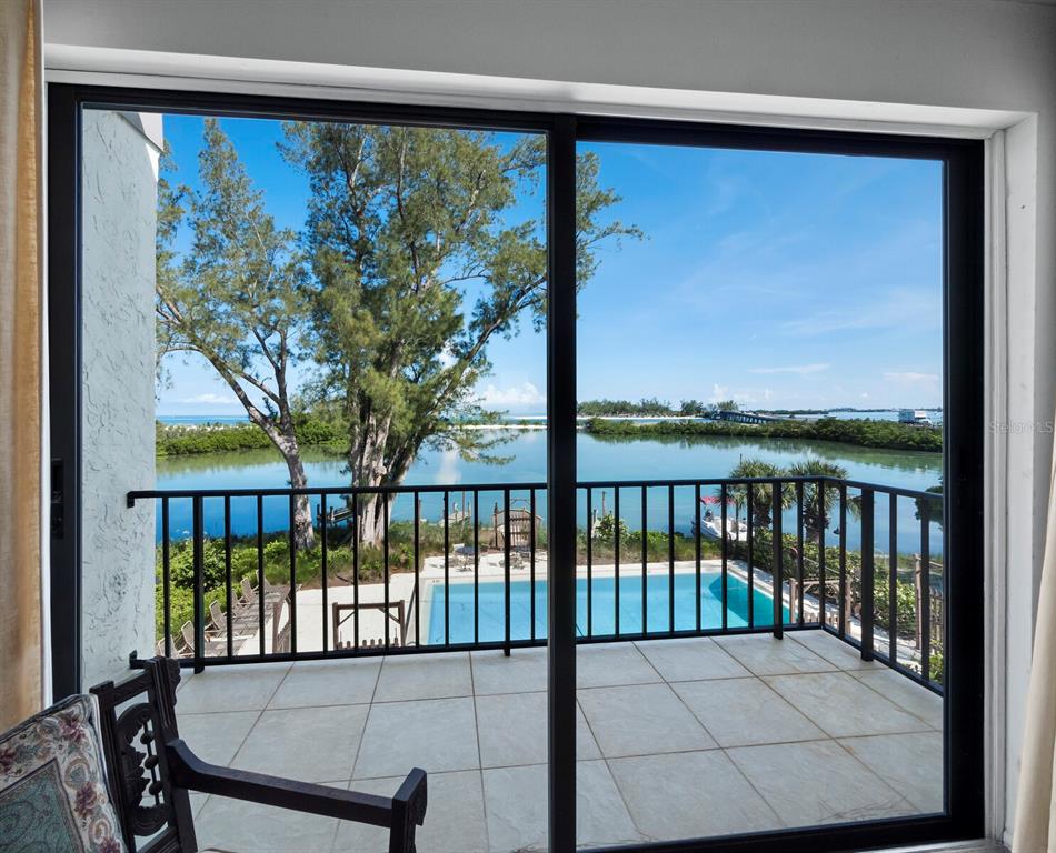 A view through sliding glass doors of a balcony, swimming pool, and waterfront landscape — 490 N SHORE ROAD UNIT 6, LONGBOAT KEY, FL