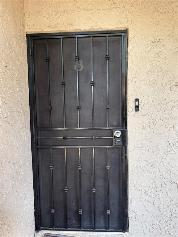 A black metal security screen door is installed on a beige stucco exterior wall — 7509 PITCH PINE CIRCLE UNIT 121, TAMPA, FL