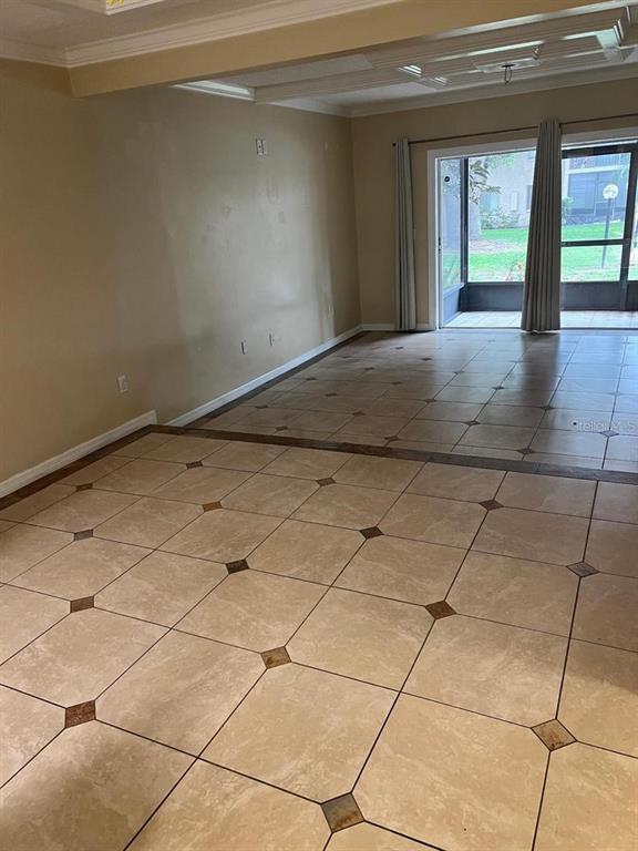 An empty room features beige tiled flooring with dark accents and a sliding glass door — 7509 PITCH PINE CIRCLE UNIT 121, TAMPA, FL