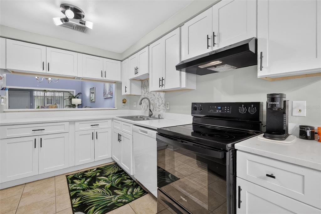 A kitchen features white cabinets, black appliances, a tile floor, and a pass-through window — 612 WOODRIDGE DRIVE, CASSELBERRY, FL