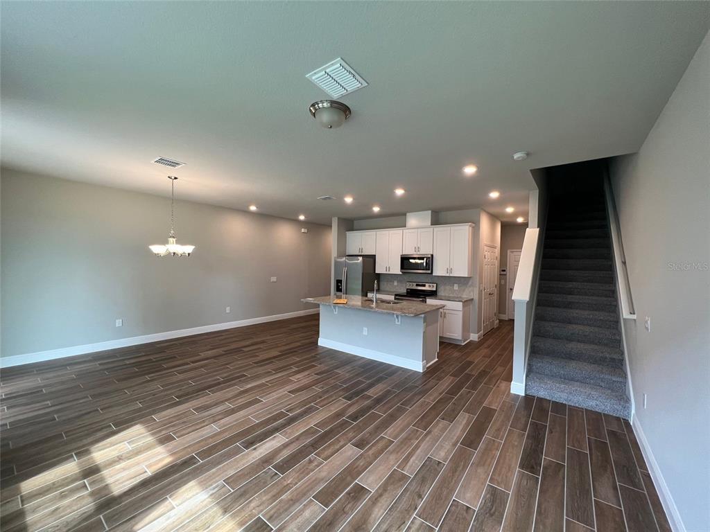 An open-concept kitchen and living area features wood-look tile flooring and a carpeted staircase — 1326 MERRYDALE WAY, WINTER PARK, FL