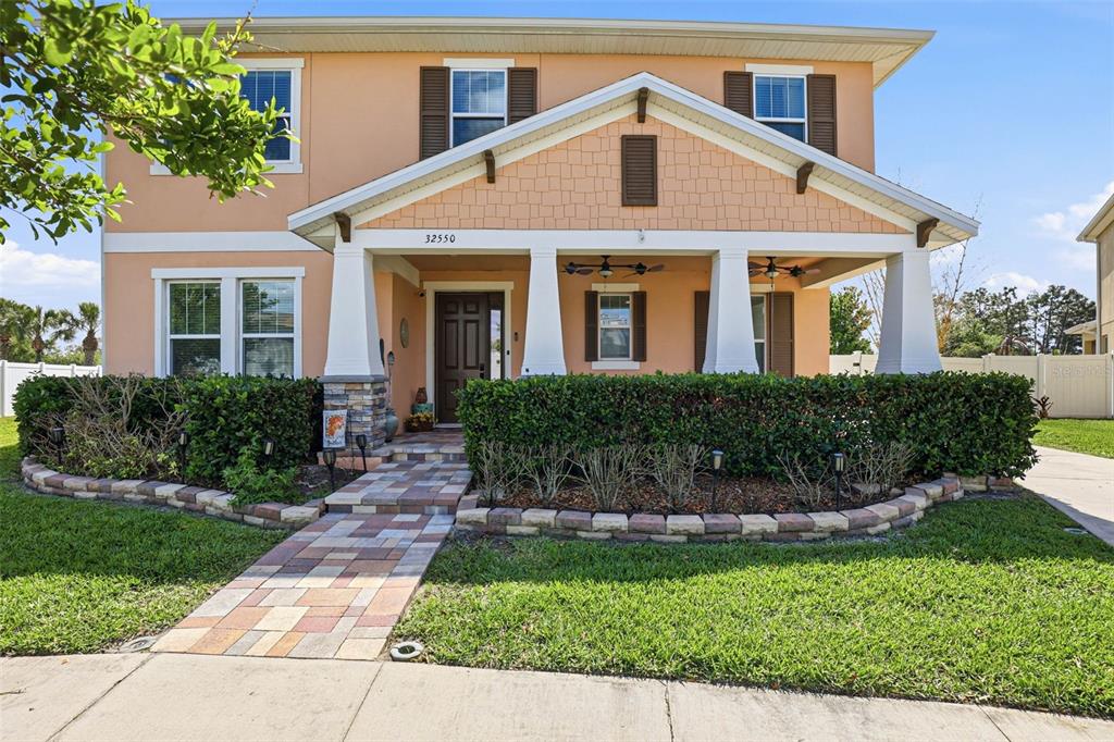 A two-story house with a peach-colored exterior, a covered front porch, and a stone-accented pillar — 32550 RAPIDS LOOP, WESLEY CHAPEL, FL