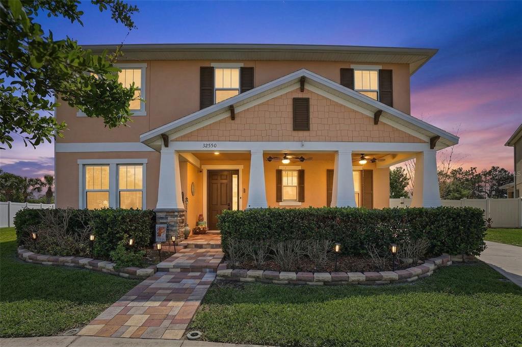 A two-story house with a covered front porch, stone accents, and a paved walkway — 32550 RAPIDS LOOP, WESLEY CHAPEL, FL