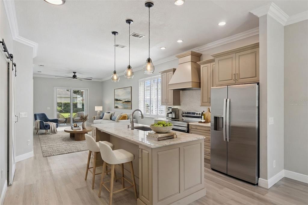 A modern kitchen with a stone-topped island and stainless steel refrigerator opens to a living area — 1206 CHESSINGTON CIRCLE, LAKE MARY, FL