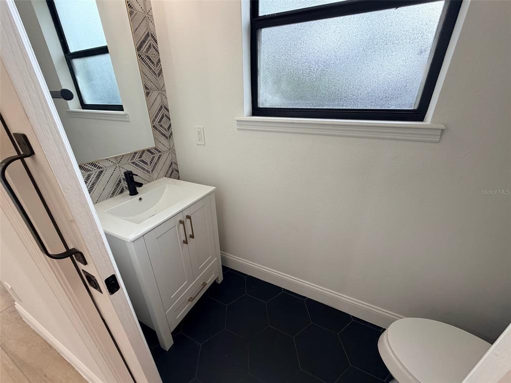 A small bathroom features a white vanity, black hexagon floor tiles, and patterned wall tile — 2013 E ESTHER STREET, ORLANDO, FL