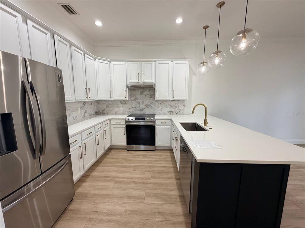 A modern kitchen features white cabinetry, stainless steel appliances, quartz countertops, and a dark island — 2013 E ESTHER STREET, ORLANDO, FL