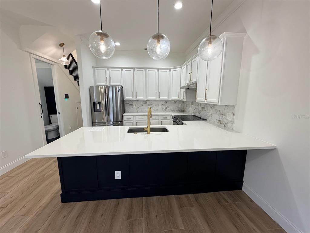 A kitchen features a dark blue island, white cabinets, gold hardware, and light wood flooring — 2013 E ESTHER STREET, ORLANDO, FL