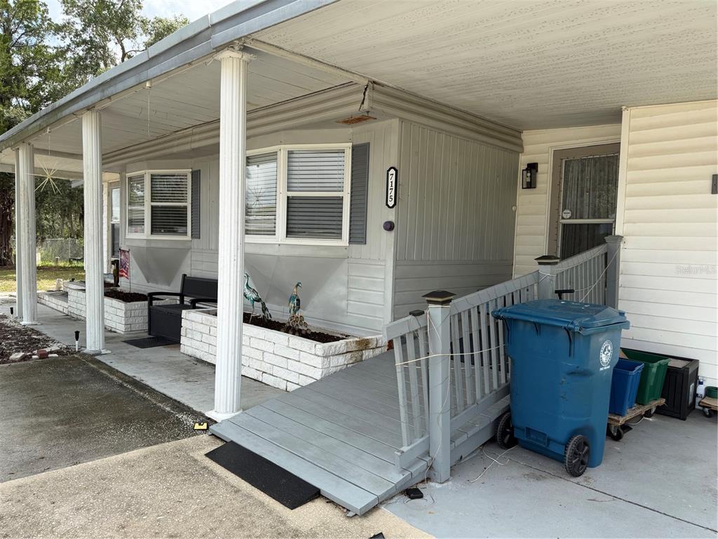 A gray mobile home exterior features a covered porch, a wooden ramp, and brick planters — 7175 FAIRLANE AVENUE, BROOKSVILLE, FL