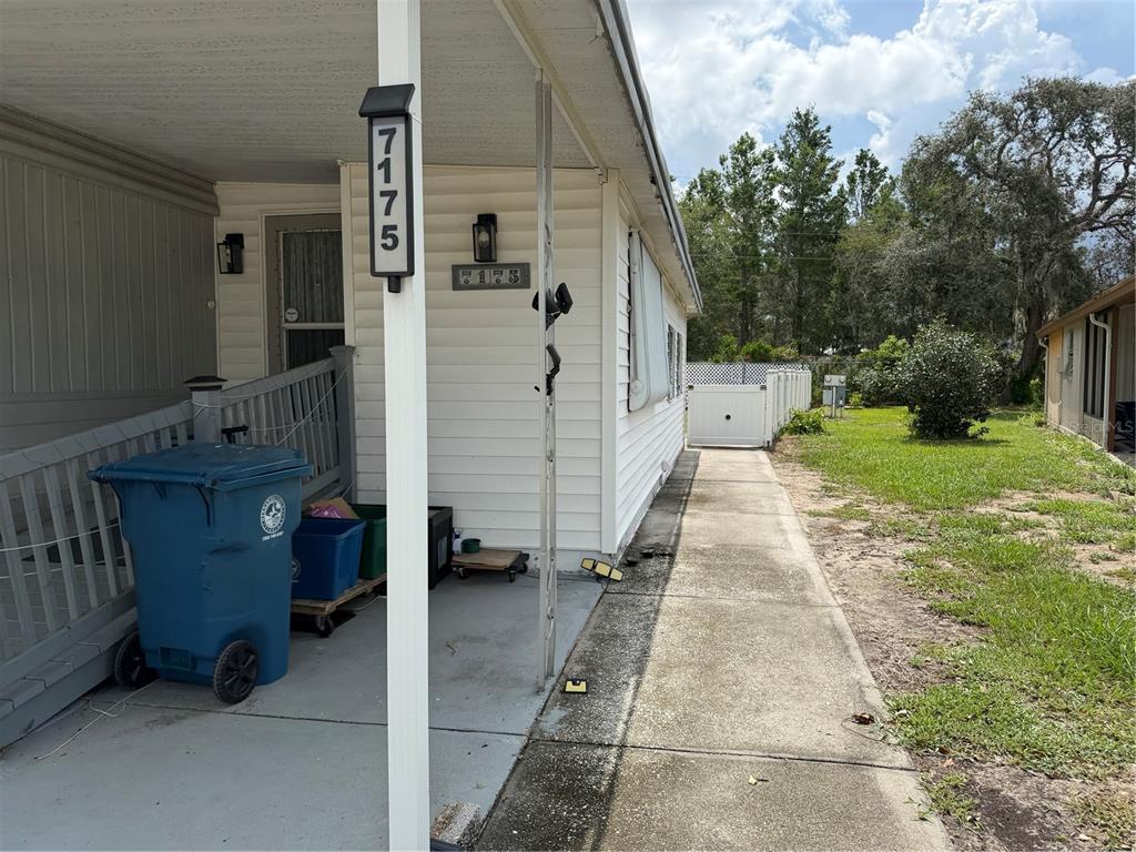 A blue trash bin sits on a concrete porch next to a white house exterior — 7175 FAIRLANE AVENUE, BROOKSVILLE, FL