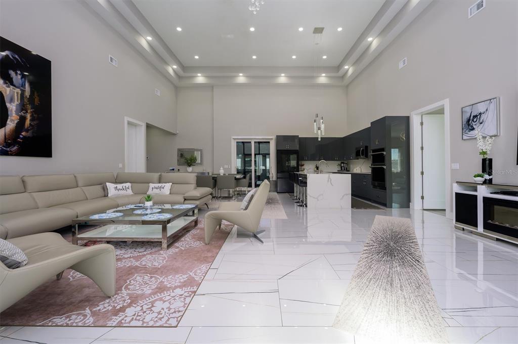 A modern open-concept living room and kitchen with high ceilings, white tile floors, and furniture — 6396 18TH STREET N, ST PETERSBURG, FL
