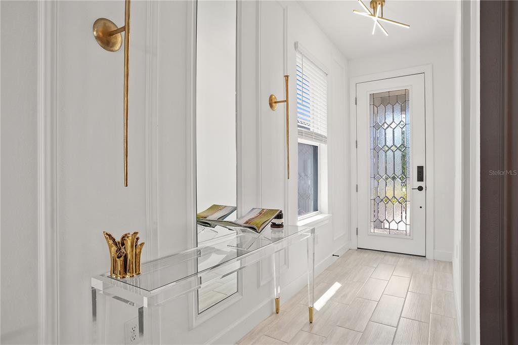 A bright entryway features a clear acrylic console table, gold wall sconces, and a glass-paneled door — 4724 CRESTPOINT WAY, PALMETTO, FL
