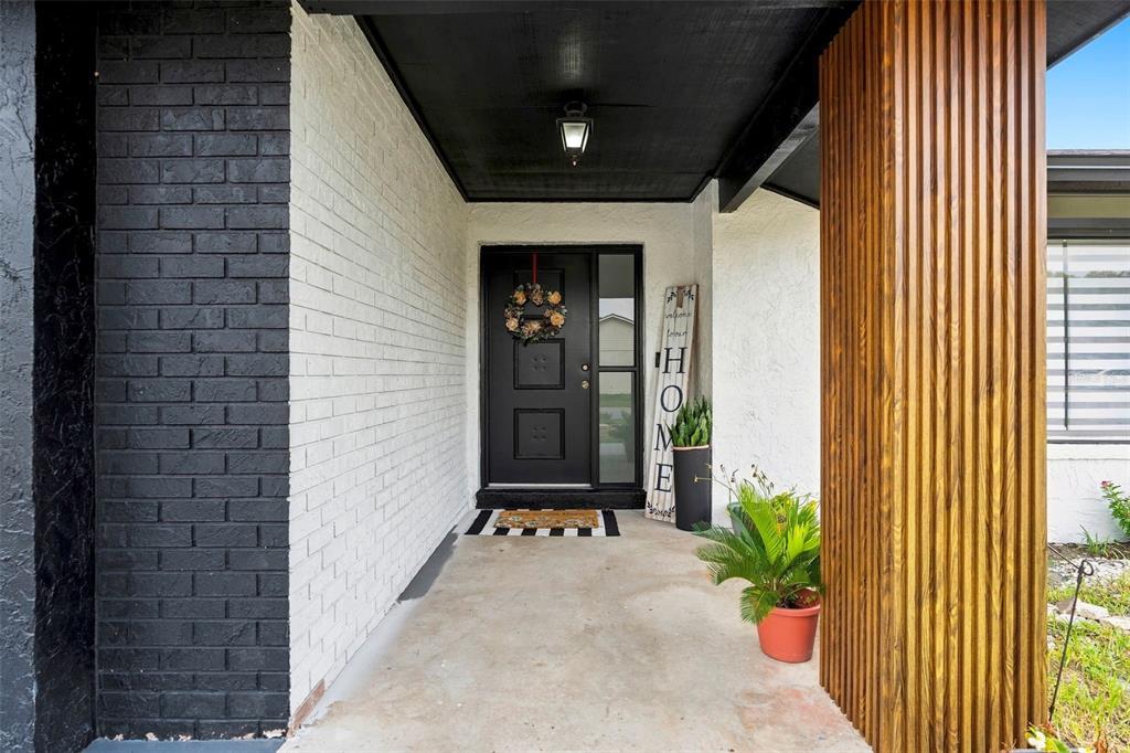 A covered front porch features a black door, white brick walls, and a wooden slat column — 10500 RAMBLEWOOD ROAD, ORLANDO, FL